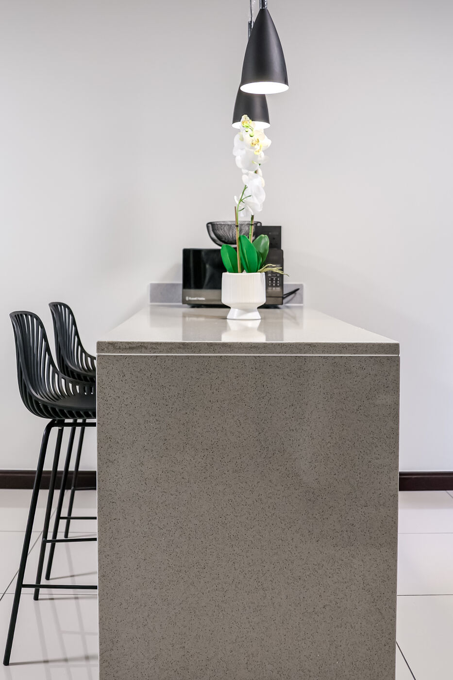 Kitchen breakfast bar in engineered stone with black bar stools and pendant lights