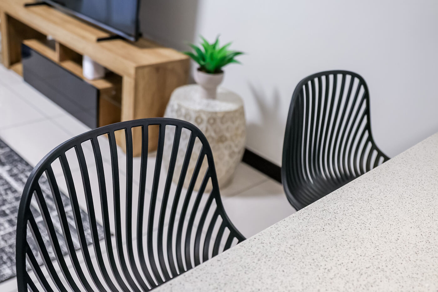 Open-plan lounge and dining area with black slatted chairs, a wooden TV unit and a leafy plant