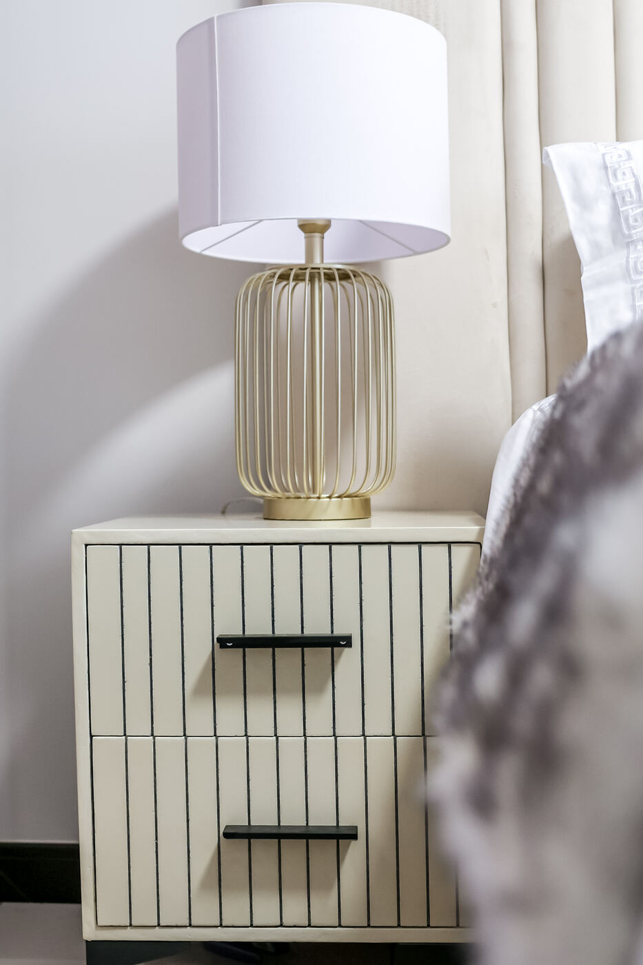 Bedside table with a gold cage lamp beside a neatly made bed